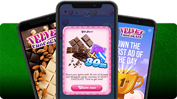 Three smartphones overlapping on a green background: the center phone shows a Candy Crush pop-up offering a 30-minute boost with Velvet Chocolate branding, while the side phones display Velvet Chocolate ads—one with almonds and chocolate pieces, the other promoting “First Ad of the Day” with a golden trophy.
