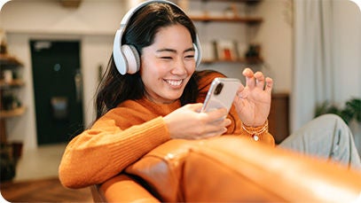 Person mit Kopfhörer und Smartphone auf einem orangefarbenen Sofa.